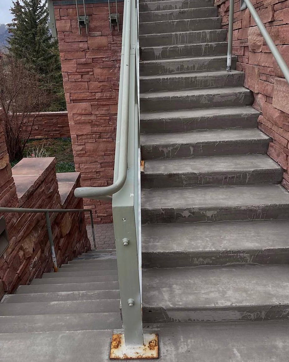 Grey concrete stairs at Mountain Village with drip stains and a rusted railing base, before